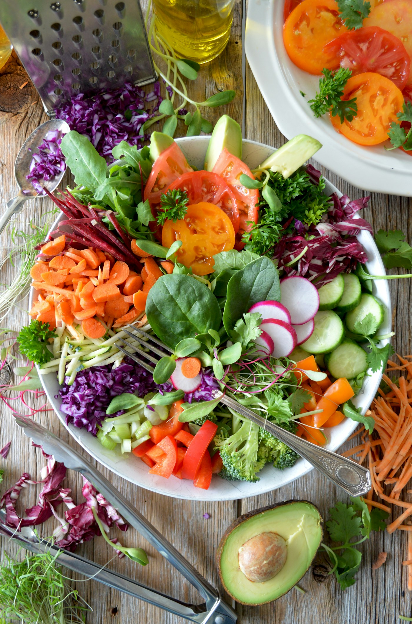 A bowl of mixed salad vegetables — greens, tomato, cucumber, avocado — on a wooden table.